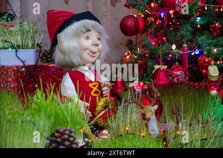 Una scena natalizia caratterizzata da una allegra statuetta di pupazzo di neve, vivaci decorazioni natalizie e vegetazione, il tutto adagiato su un albero decorato di rosso Foto Stock