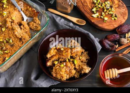 Colazione al forno mediorientale: Casseruola preparata con bulgur, uova, latte, datteri e spezie con pistacchi tritati e miele sgocciolato Foto Stock