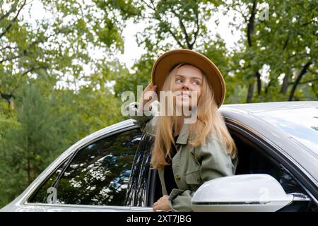 Donna bionda con cappello che sporge la testa dalla vettura del parabrezza. I giovani turisti esplorano i viaggi locali, trasformandoli in momenti autentici. Emozioni vere espressioni di fuga e di rinfrescarsi rilassarsi all'aria aperta e pulita Foto Stock