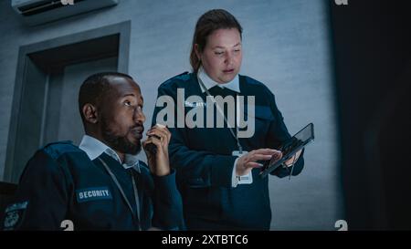 Un agente di sicurezza donna sta in piedi e utilizza un tablet. Un dispatcher afroamericano parla in walkie talkie. Gli operatori di sorveglianza multietnica controllano le telecamere a circuito chiuso nel moderno centro di monitoraggio. Foto Stock