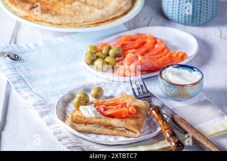 Pancake con gravlax, formaggio fresco e olive su sfondo chiaro. Un piatto tradizionale per Maslenitsa o Carnevale. Messa a fuoco selettiva. Foto Stock