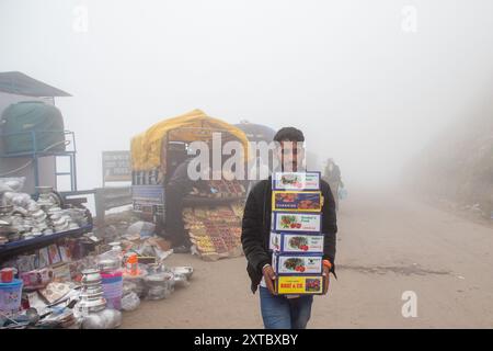 Peer Ki Gali, India, 14/08/2024, Un ragazzo del Kashmir che vende scatole di frutta in mezzo a una fitta nebbia vicino al passo PIR Panjal, chiamato anche Peer Ki Gali, a circa 100 km a sud di Srinagar, la capitale estiva di Jammu e Kashmir. Il passo PIR Panjal è un passo di montagna e una destinazione turistica situata nella catena PIR Panjal di Jammu e Kashmir, che collega la valle del Kashmir ai distretti di Rajouri e Punch tramite Mughal Road. È il punto più alto della strada Mughal a 3.490 metri sul livello del mare. Mughal Road, come suggerisce il nome, è stata storicamente creata e utilizzata dagli imperatori moghul. Era la strada che percorreva Foto Stock