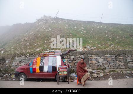 Peer Ki Gali, India, 14/08/2024, Un uomo del Kashmir vide vendere scialli in mezzo a una fitta nebbia vicino al passo PIR Panjal, chiamato anche Peer Ki Gali, a circa 100 km a sud di Srinagar, la capitale estiva di Jammu e Kashmir. Il passo PIR Panjal è un passo di montagna e una destinazione turistica situata nella catena PIR Panjal di Jammu e Kashmir, che collega la valle del Kashmir ai distretti di Rajouri e Punch tramite Mughal Road. È il punto più alto della strada Mughal a 3.490 metri sul livello del mare. Mughal Road, come suggerisce il nome, è stata storicamente creata e utilizzata dagli imperatori moghul. Era la strada che percorreva Foto Stock