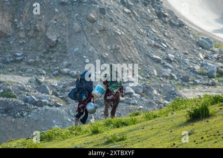 Peer Ki Gali, India, 14/08/2024, le donne kashmiri trasportano secchi vuoti per raccogliere acqua durante una giornata di sole vicino al passo PIR Panjal, chiamato anche Peer Ki Gali, a circa 100 km a sud di Srinagar, la capitale estiva di Jammu e Kashmir. Il passo PIR Panjal è un passo di montagna e una destinazione turistica situata nella catena PIR Panjal di Jammu e Kashmir, che collega la valle del Kashmir ai distretti di Rajouri e Punch tramite Mughal Road. È il punto più alto della strada Mughal a 3.490 metri sul livello del mare. Mughal Road, come suggerisce il nome, è stata storicamente creata e utilizzata dagli imperatori moghul. IT Foto Stock