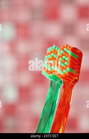 Due spazzolini, uno verde e uno arancione, su sfondo rosa sfocato. Mostra le attrezzature per l'igiene quotidiana Foto Stock