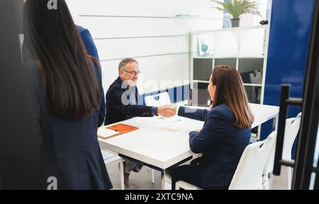 Colleghi multigenerazionali che lavorano all'interno dell'ufficio immobiliare - imprenditori persone che stringono la mano durante la chiusura di affari - obiettivo principale o Foto Stock