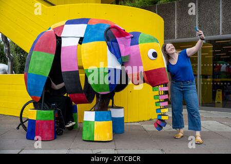 Londra, Regno Unito. 14 agosto 2024. Yvonne Stone, burattinaio e regista, con Elmer, l'elefante patchwork, un burattino gigante, che fa la sua prima apparizione pubblica mentre sfilano fuori dal Southbank Centre, prima di prendere parte al magico adattamento musicale di Tall Stories degli amatissimi libri di Elmer di David McKee. Gli spettacoli si terranno al Lowry di Salford e al Southbank Centre in ottobre. Crediti: Stephen Chung / Alamy Live News Foto Stock