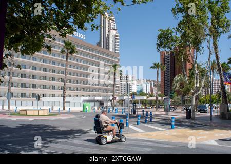 Uomo che attraversa la zebra a bordo di uno scooter elettrico di fronte a un hotel a Benidorm, provincia di Alicante, Spagna Foto Stock