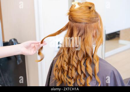 Una donna con i capelli ricci sta facendo i capelli da uno stilista. Lo stilista sta tenendo i capelli della donna mentre la donna si siede su una sedia Foto Stock