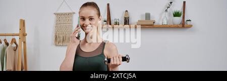 Una donna in abiti da allenamento sorride mentre solleva pesi e parla al telefono. Foto Stock