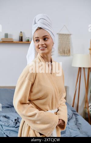 Una giovane donna con un accappatoio e un asciugamano sulla testa sta nella sua camera da letto. Foto Stock