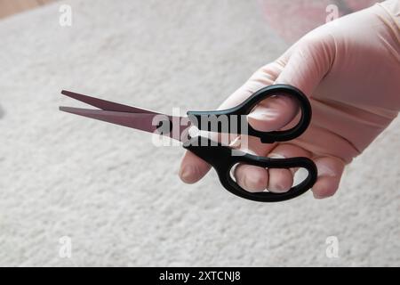 Forbici in mano con guanto in gomma. Cesoie in acciaio per il taglio. Foto Stock