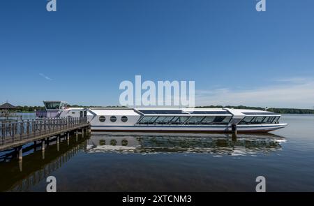 Neuruppin, Germania. 12 agosto 2024. Un'escursione in barca è ormeggiata presso un molo sulla passeggiata sul lago Ruppin. Crediti: Monika Skolimowska/dpa/Alamy Live News Foto Stock