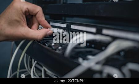 L'amministratore di sistema maschio collega i cavi al rack server che funziona nella sala server. Manutenzione di reti locali o server Web. Funzionamento dei sistemi e delle reti di informazione. Data storage center. Foto Stock