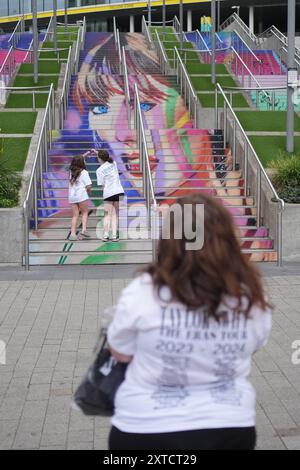 (Da sinistra a destra) Gracie Hiles di otto anni e la sorella di dodici anni Jessica Evans, si pongono come la loro madre (nome non dato) scatta la loro fotografia ai gradini Swiftie e ai murales di Wembley Park, a nord-ovest di Londra, in vista del concerto dell'era Tour di Taylor Swift giovedì. Data foto: Mercoledì 14 agosto 2024. Foto Stock