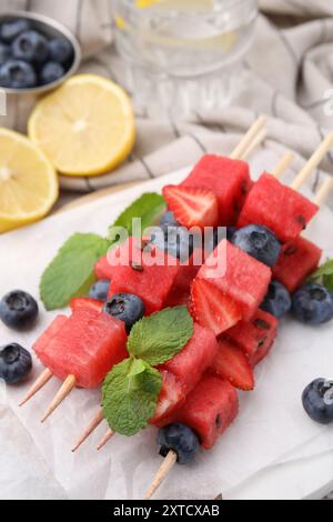 Spiedini con gustosi anguria, fragole, mirtilli e menta sul tavolo, primo piano Foto Stock