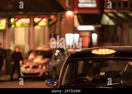 Una vista ritagliata di un taxi britannico, con la luce DEL TAXI accesa, che indica che è disponibile, con la vista della strada sullo sfondo leggermente fuori fuoco Foto Stock