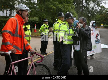 Leicester, Leicestershire, Regno Unito. 14 agosto 2024. Gli agenti di polizia cercano di tenere i manifestanti dell'autostrada durante la dimostrazione. I manifestanti si riuniscono fuori dai cancelli della fabbrica Elbit System a Leicester. Gli operatori sanitari per la Palestina si sono Uniti alla manifestazione molti di loro nei loro scrub per protestare mentre i lavoratori venivano a lavorare presso la compagnia israeliana di armi. I manifestanti protestano contro le armi fabbricate in questa fabbrica che ritengono vengano successivamente utilizzate per opprimere i palestinesi a Gaza e altrove. Il 85% della flotta israeliana di droni è fornito da Elbit Systems e i manifestanti vogliono i loro sette Foto Stock