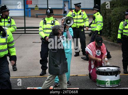 Leicester, Leicestershire, Regno Unito. 14 agosto 2024. Gli agenti di polizia stanno tra i manifestanti e il cancello della fabbrica della Elbit Systems durante la dimostrazione. I manifestanti si riuniscono fuori dai cancelli della fabbrica Elbit System a Leicester. Gli operatori sanitari per la Palestina si sono Uniti alla manifestazione molti di loro nei loro scrub per protestare mentre i lavoratori venivano a lavorare presso la compagnia israeliana di armi. I manifestanti protestano contro le armi fabbricate in questa fabbrica che ritengono vengano successivamente utilizzate per opprimere i palestinesi a Gaza e altrove. Il 85% della flotta di droni israeliani è fornito da Elbit Systems A. Foto Stock