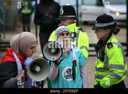 Leicester, Leicestershire, Regno Unito. 14 agosto 2024. Gli agenti di polizia stanno tra i manifestanti e il cancello della fabbrica della Elbit Systems durante la dimostrazione. I manifestanti si riuniscono fuori dai cancelli della fabbrica Elbit System a Leicester. Gli operatori sanitari per la Palestina si sono Uniti alla manifestazione molti di loro nei loro scrub per protestare mentre i lavoratori venivano a lavorare presso la compagnia israeliana di armi. I manifestanti protestano contro le armi fabbricate in questa fabbrica che ritengono vengano successivamente utilizzate per opprimere i palestinesi a Gaza e altrove. Il 85% della flotta di droni israeliani è fornito da Elbit Systems A. Foto Stock