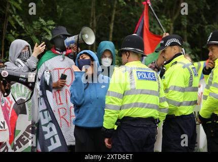 Leicester, Leicestershire, Regno Unito. 14 agosto 2024. I manifestanti si trovano di fronte alla fabbrica gridando e tenendo striscioni trattenuti da un cordone di polizia durante la dimostrazione. I manifestanti si riuniscono fuori dai cancelli della fabbrica Elbit System a Leicester. Gli operatori sanitari per la Palestina si sono Uniti alla manifestazione molti di loro nei loro scrub per protestare mentre i lavoratori venivano a lavorare presso la compagnia israeliana di armi. I manifestanti protestano contro le armi fabbricate in questa fabbrica che ritengono vengano successivamente utilizzate per opprimere i palestinesi a Gaza e altrove. Il 85% della flotta israeliana di droni è fornito da El Foto Stock