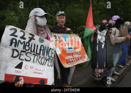 Leicester, Leicestershire, Regno Unito. 14 agosto 2024. I manifestanti stanno di fronte alla fabbrica gridando e tenendo dei cartelli durante la dimostrazione. I manifestanti si riuniscono fuori dai cancelli della fabbrica Elbit System a Leicester. Gli operatori sanitari per la Palestina si sono Uniti alla manifestazione molti di loro nei loro scrub per protestare mentre i lavoratori venivano a lavorare presso la compagnia israeliana di armi. I manifestanti protestano contro le armi fabbricate in questa fabbrica che ritengono vengano successivamente utilizzate per opprimere i palestinesi a Gaza e altrove. Il 85% della flotta israeliana di droni è fornito da Elbit Systems e i manifestanti vogliono Foto Stock