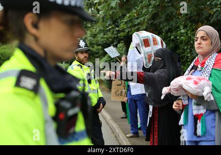 Leicester, Leicestershire, Regno Unito. 14 agosto 2024. I manifestanti stanno di fronte alla fabbrica gridando e puntando durante la dimostrazione. I manifestanti si riuniscono fuori dai cancelli della fabbrica Elbit System a Leicester. Gli operatori sanitari per la Palestina si sono Uniti alla manifestazione molti di loro nei loro scrub per protestare mentre i lavoratori venivano a lavorare presso la compagnia israeliana di armi. I manifestanti protestano contro le armi fabbricate in questa fabbrica che ritengono vengano successivamente utilizzate per opprimere i palestinesi a Gaza e altrove. Il 85% della flotta israeliana di droni è fornito da Elbit Systems e i manifestanti vogliono il loro Foto Stock