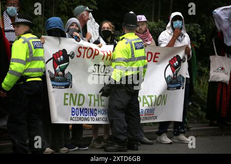 Leicester, Leicestershire, Regno Unito. 14 agosto 2024. I manifestanti si trovano di fronte alla fabbrica gridando e tenendo striscioni trattenuti da un cordone di polizia durante la dimostrazione. I manifestanti si riuniscono fuori dai cancelli della fabbrica Elbit System a Leicester. Gli operatori sanitari per la Palestina si sono Uniti alla manifestazione molti di loro nei loro scrub per protestare mentre i lavoratori venivano a lavorare presso la compagnia israeliana di armi. I manifestanti protestano contro le armi fabbricate in questa fabbrica che ritengono vengano successivamente utilizzate per opprimere i palestinesi a Gaza e altrove. Il 85% della flotta israeliana di droni è fornito da El Foto Stock