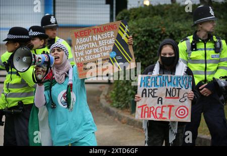 Leicester, Leicestershire, Regno Unito. 14 agosto 2024. I manifestanti tengono dei cartelli e cantano davanti ai cancelli della fabbrica durante la dimostrazione. I manifestanti si riuniscono fuori dai cancelli della fabbrica Elbit System a Leicester. Gli operatori sanitari per la Palestina si sono Uniti alla manifestazione molti di loro nei loro scrub per protestare mentre i lavoratori venivano a lavorare presso la compagnia israeliana di armi. I manifestanti protestano contro le armi fabbricate in questa fabbrica che ritengono vengano successivamente utilizzate per opprimere i palestinesi a Gaza e altrove. Il 85% della flotta israeliana di droni è fornito da Elbit Systems e i manifestanti vogliono il Foto Stock