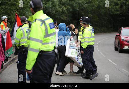 Leicester, Leicestershire, Regno Unito. 14 agosto 2024. I manifestanti cercano di entrare in strada per impedire che i lavoratori arrivino trattenuti dagli agenti di polizia durante la manifestazione. I manifestanti si riuniscono fuori dai cancelli della fabbrica Elbit System a Leicester. Gli operatori sanitari per la Palestina si sono Uniti alla manifestazione molti di loro nei loro scrub per protestare mentre i lavoratori venivano a lavorare presso la compagnia israeliana di armi. I manifestanti protestano contro le armi fabbricate in questa fabbrica che ritengono vengano successivamente utilizzate per opprimere i palestinesi a Gaza e altrove. Il 85% della flotta israeliana di droni è fornita da Elbit Sy Foto Stock