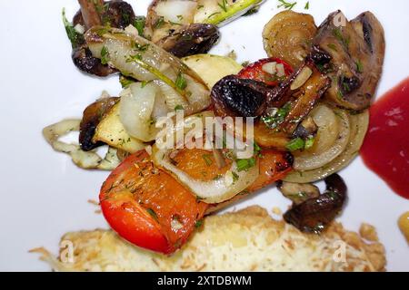 Un colorato mix di verdure alla griglia, tra cui funghi, cipolle e peperoni, guarnite e disposte ordinatamente su un piatto bianco. Foto Stock