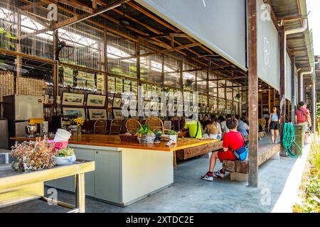 Le persone si siedono e mangiano ad un grande tavolo di legno. Da un lato, i dipinti ad acquerello sono esposti in vendita nel deposito degli autobus Hin, George Town, Penang Foto Stock