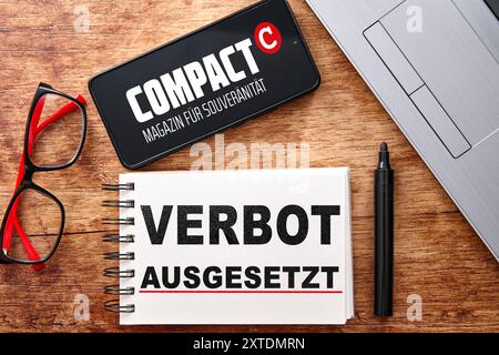 Baviera, Germania - 14 agosto 2024: Su una scrivania si trova uno smartphone con il logo della rivista Compact, un portatile e un blocco note con un'iscrizione: Ban Suspended. Immagine simbolica sentenza della Corte del 14 agosto, il divieto di Compact-Magazin GmbH è stato parzialmente revocato. FOTOMONTAGGIO *** Auf einem Schreibtisch liegt ein smartphone mit dem Logo vom Compact Magazin, danaben ein laptop e ein Notizblock mit Aufschrift: Verbot ausgesetzt. Symbolbild Gerichtsurteil vom 14 agosto, das Verbot der Compact-Magazin GmbH wurde teilweise aufgehoben. FOTOMONTAGE Foto Stock