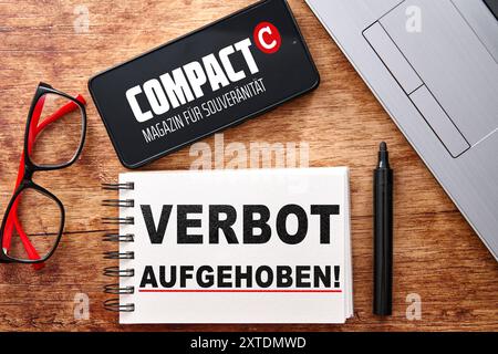 Baviera, Germania - 14 agosto 2024: Su una scrivania si trova uno smartphone con il logo della rivista Compact, un portatile e un blocco note con un'iscrizione: Ban Lift. Immagine simbolica sentenza della Corte del 14 agosto, il divieto di Compact-Magazin GmbH è stato parzialmente sospeso. FOTOMONTAGGIO *** Auf einem Schreibtisch liegt ein smartphone mit dem Logo vom Compact Magazin, danaben ein laptop e ein Notizblock mit Aufschrift: Verbot aufgehoben. Symbolbild Gerichtsurteil vom 14 agosto, das Verbot der Compact-Magazin GmbH wurde teilweise ausgesetzt. FOTOMONTAGE Foto Stock