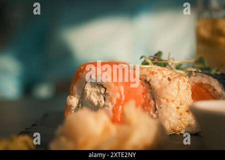 Sushi roll con un pezzo di salmone sopra. Zenzero sottaceto in primo piano. Mettere a fuoco lo sfondo in cui sono posizionati i sushi roll. Una scena di relax Foto Stock