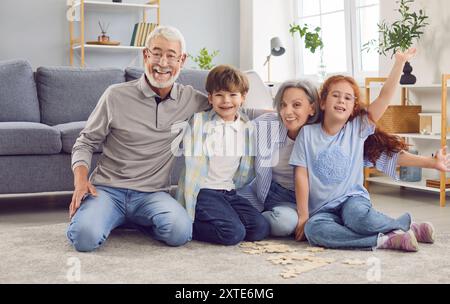 Nonna, nonno e nipoti che giocano sul pavimento in un puzzle a casa Foto Stock
