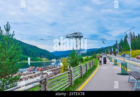 Goditi la passeggiata lungo il lago Molodista con vista sulle verdi montagne, zipline e panchine per i turisti, Bukovel, Ucraina Foto Stock