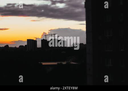 Sagome di edifici alti, gru da costruzione contro un cielo nuvoloso al tramonto. Cantiere. Progetto tecnico. Sviluppo e alloggi. Foto Stock