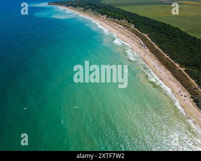 Vista aerea di una spiaggia sabbiosa con tende sparse e ombrelloni lungo la costa. Le onde si bagnano delicatamente sulla riva, catturando un tranquillo e. Foto Stock