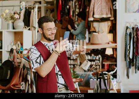 Uomo sorridente che tiene il cappello e usa lo smartphone Foto Stock