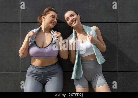 Due giovani donne in abbigliamento sportivo in piedi vicino al muro e riposano dopo l'allenamento Foto Stock