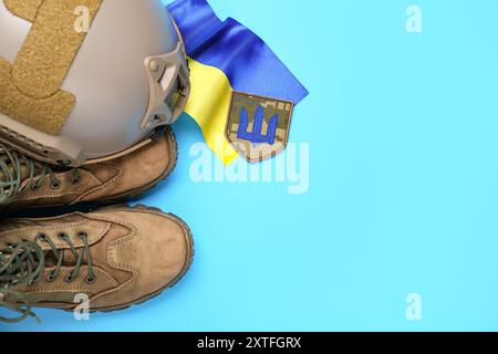 Distintivo con tridente, stivali militari, casco tattico e bandiera Ucraina su sfondo blu Foto Stock