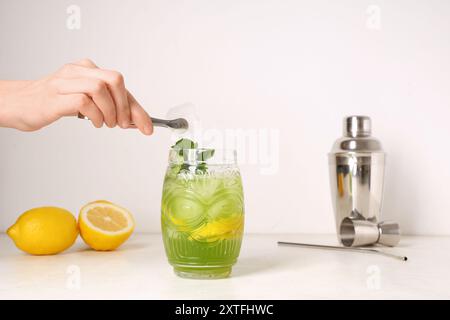 Mano femminile con un bicchiere di gustosa limonata, limoni e menta su sfondo bianco Foto Stock