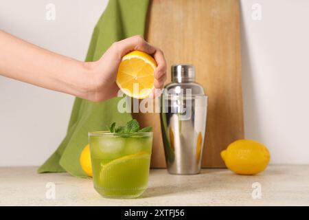 Donna che spreme il succo di limone in una gustosa limonata su sfondo bianco Foto Stock