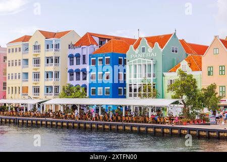 Edifici colorati sul lungomare a Willemstad, con ristoranti all'aperto lungo l'acqua, caratterizzati da un'atmosfera vivace e vibrante nelle giornate di sole. Foto Stock
