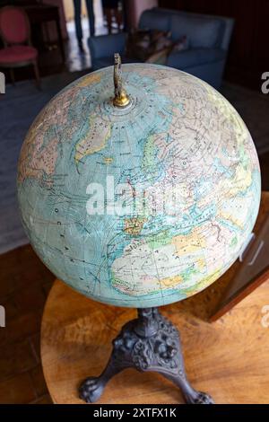 Un antico globo raffigurante la mappa del mondo posizionato su una superficie di legno vicino a una finestra con tende. Foto Stock
