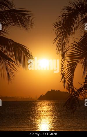 Uno splendido tramonto sull'oceano incorniciato da palme con sagome di colline lontane Foto Stock
