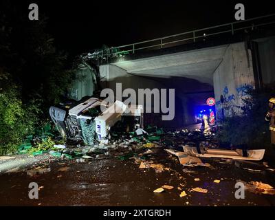 Bad Oeynhausen, Germania. 14 agosto 2024. I vigili del fuoco stanno lavorando sul luogo di un incidente dopo che un camion è caduto da un ponte autostradale. Un camionista ha schiantato il suo trattore da un ponte su una strada sottostante sulla Autobahn 2 verso Hannover nel distretto di Minden-Lübbecke e ha subito gravi lesioni. Secondo le informazioni attuali, aveva perso il controllo del suo veicolo a causa dell'aquaplaning dopo una forte pioggia vicino a Bad Oeynhausen, ha detto la polizia. Crediti: Christian Müller/Westfalennews/dpa/Alamy Live News Foto Stock