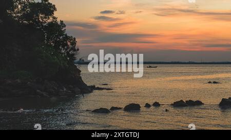 Balikpapan, Indonesia - 15 giugno 2024. Un'immagine tranquilla di un vibrante tramonto sulla superficie dell'oceano, con la silhouette di una barca e di una nave. Foto Stock