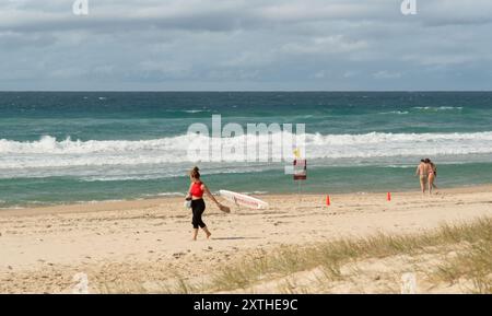 Persone non identificate su una spiaggia sabbiosa con segnali di avvertimento bagnino a Surfers Paradise, Queensland, Australia, 11 agosto 2024. Foto Stock